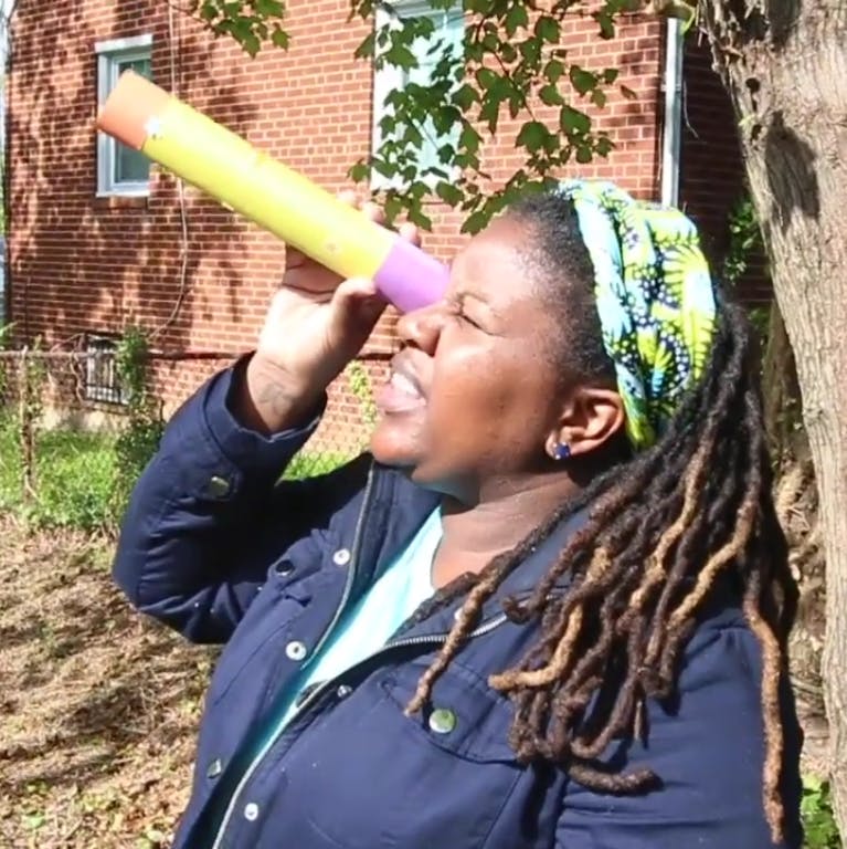 Domonique holds a telescope up to one of her eyes and looks at the sky.