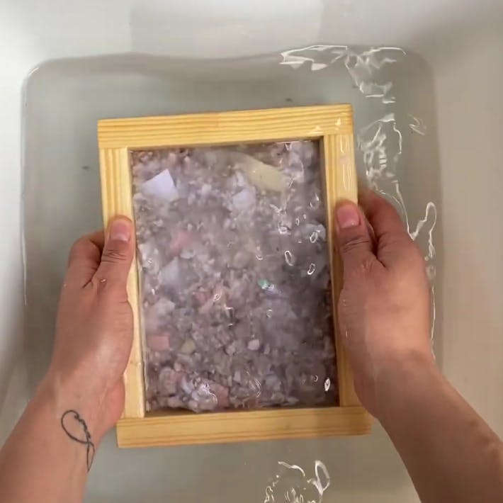 Pic of hands holding a mold and deckle, making a sheet of homemade paper
