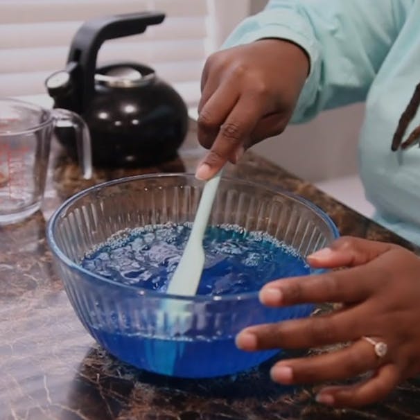 Domonique stirs the blue jello in a clear bowl.