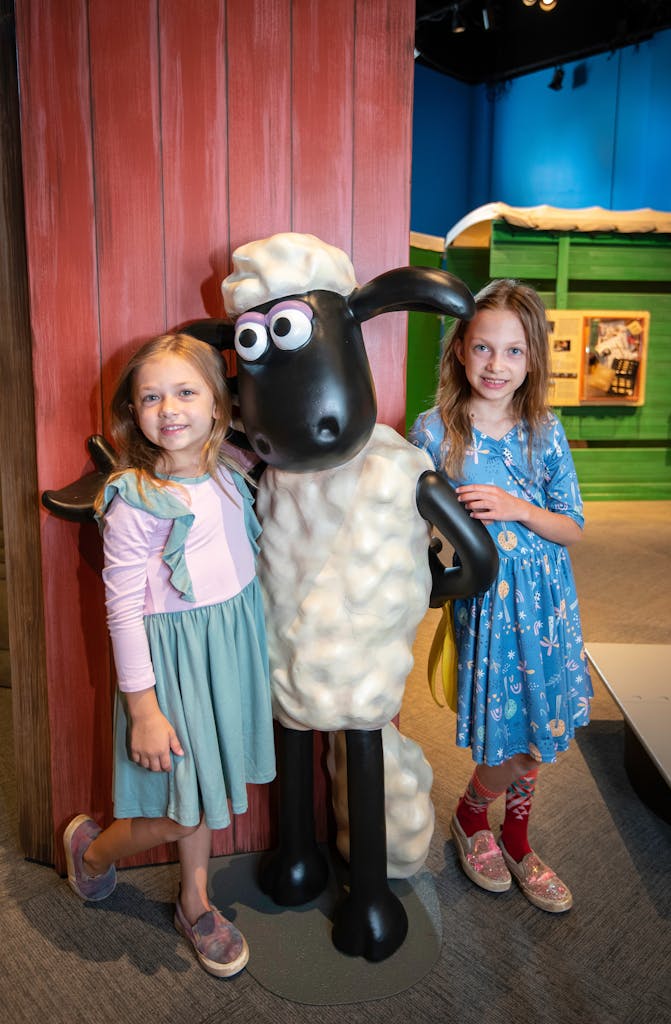 Two girls smiling next to Shaun the Sheep