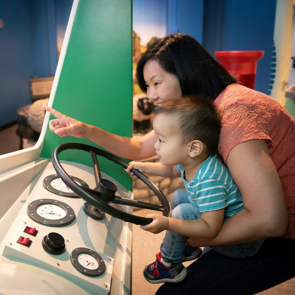Mother and young boy engaging in imaginative play at the wheel of a truck