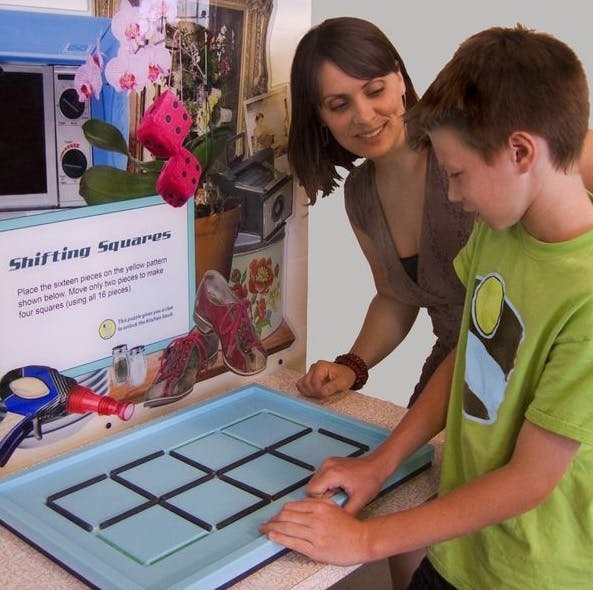A young boy and a middle-aged woman look down at a blue rectangle with dark squares on it.