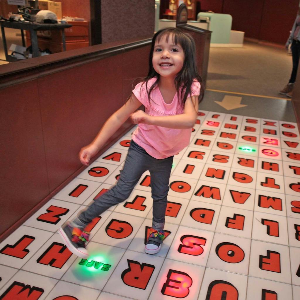 A toddler dances on a floor covered in red letter tiles.