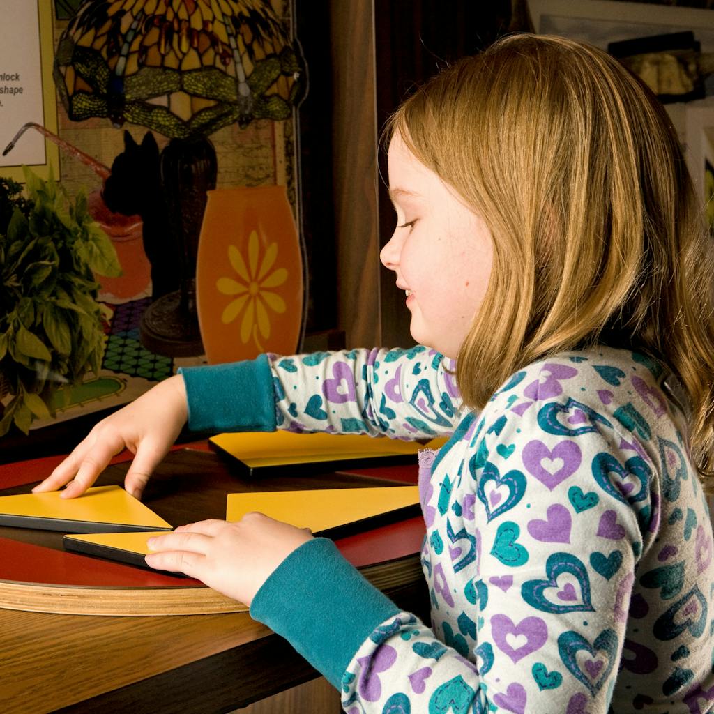 A young girl looks down as she moves yellow triangles on a red table.